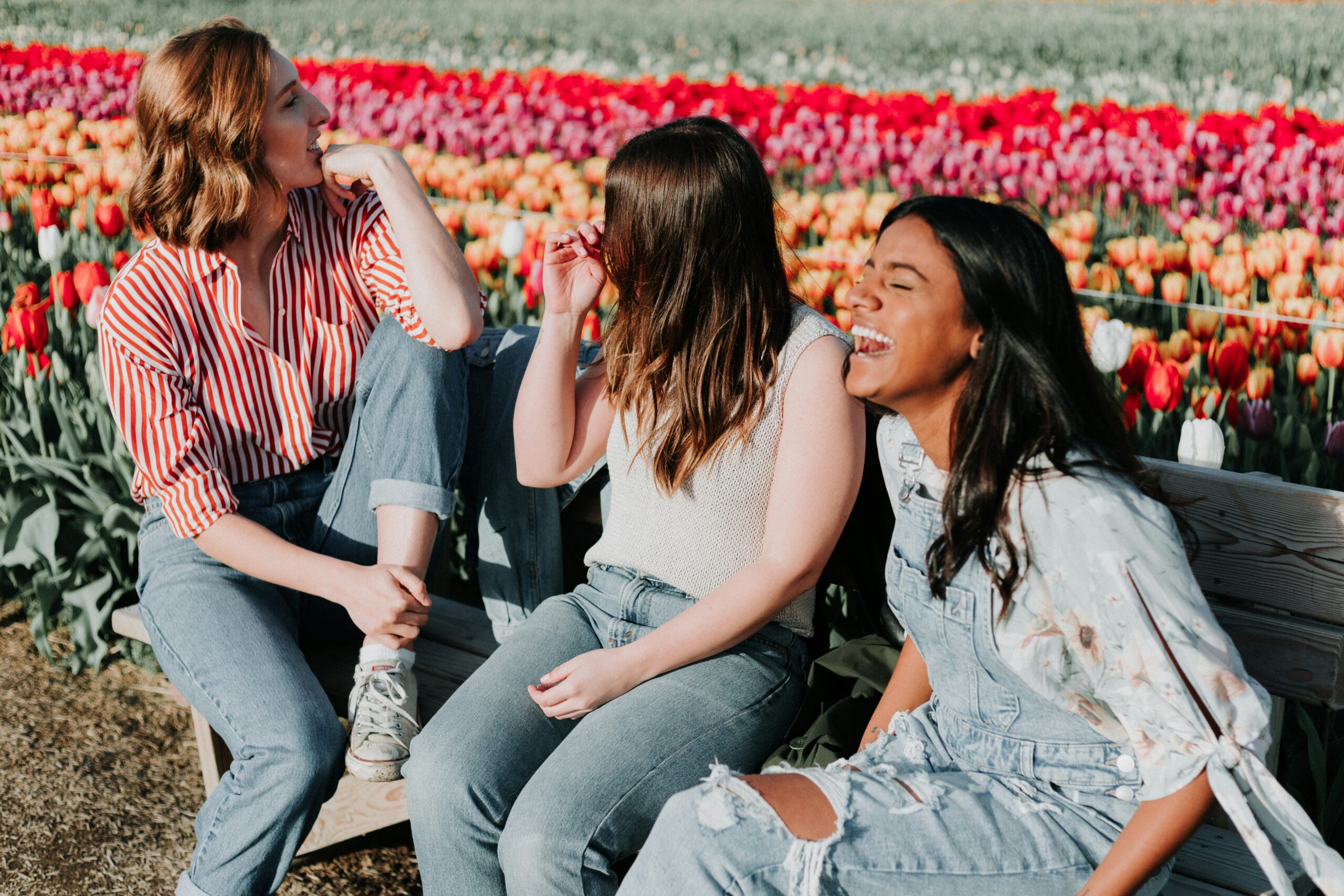 Three women laughing together in front of a field of tulips.