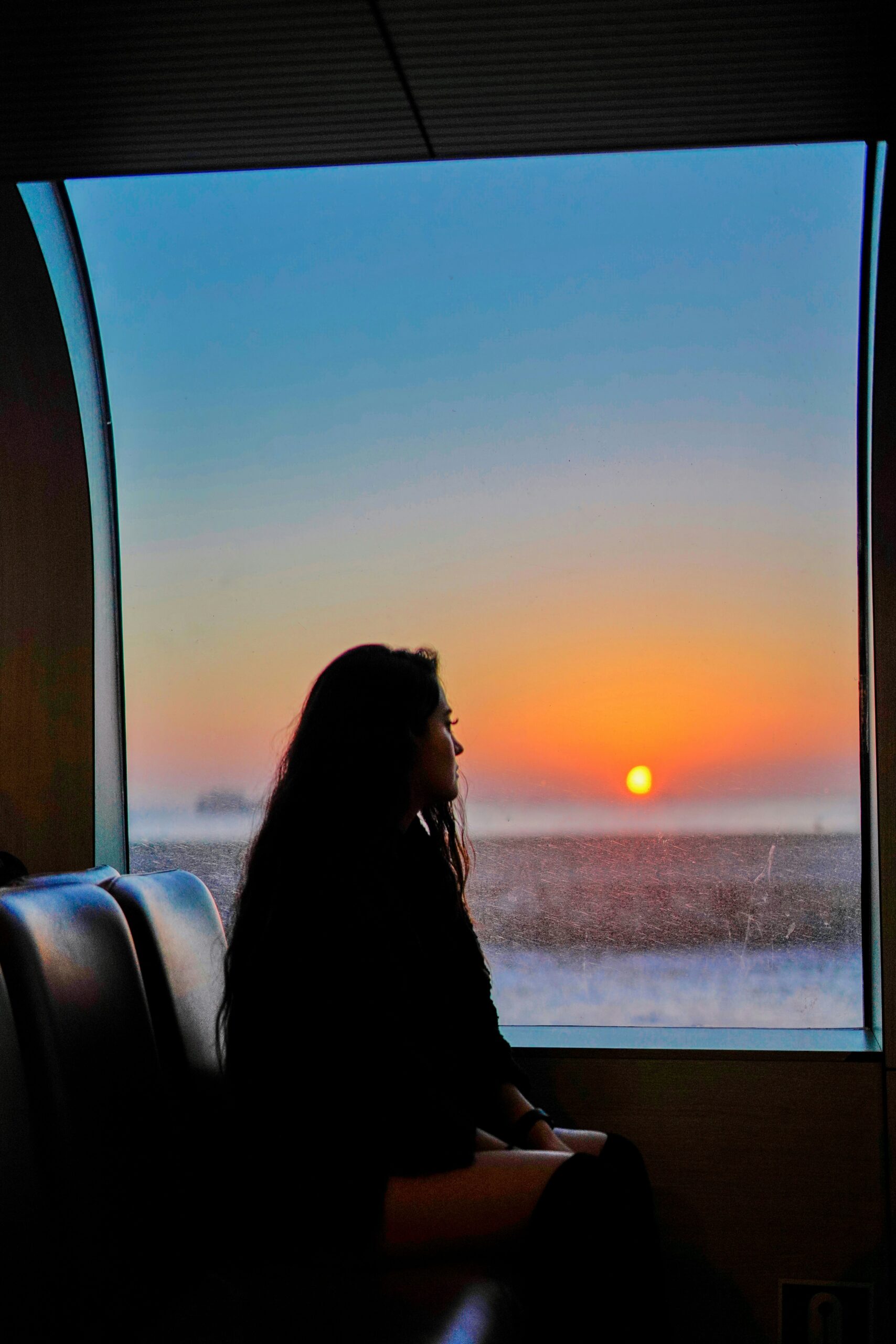 Woman looking out window on train at sunset.