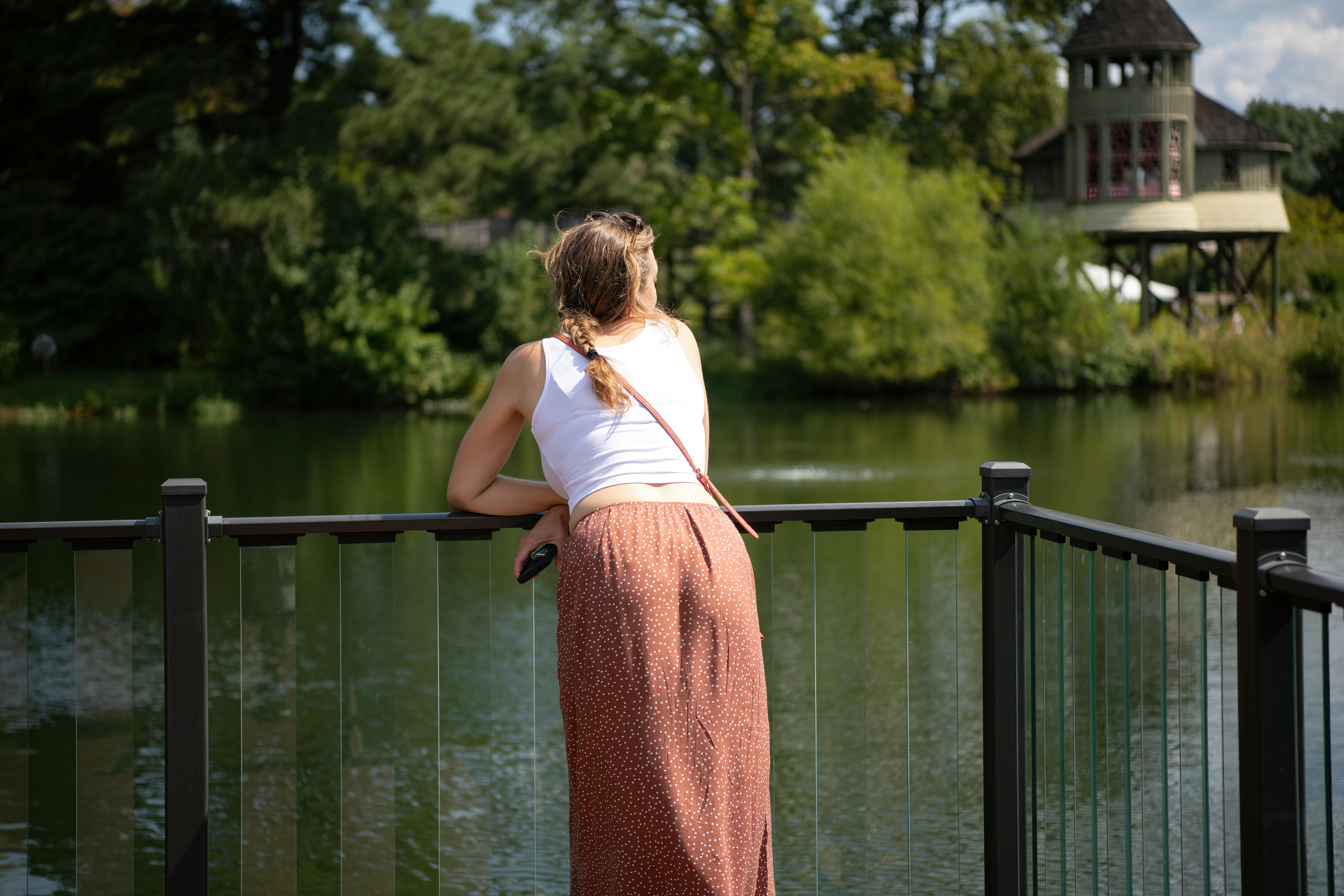 Woman leaning on railing and looking out at water and trees.